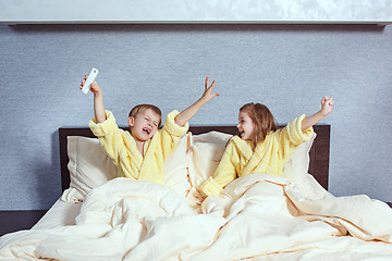 Image showing Happy laughing kids, boy and girl in soft bathrobe after bath play on white bed