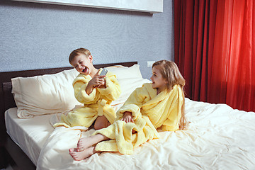 Image showing Happy laughing kids, boy and girl in soft bathrobe after bath play on white bed