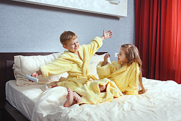 Image showing Happy laughing kids, boy and girl in soft bathrobe after bath play on white bed