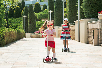 Image showing Preschooler girls riding scooter outdoors.