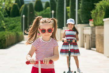 Image showing Preschooler girls riding scooter outdoors.