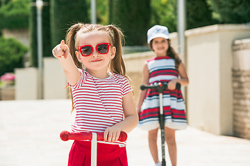 Image showing Preschooler girls riding scooter outdoors.