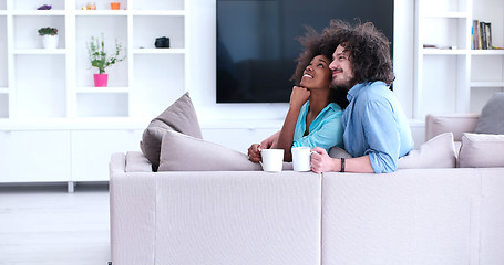 Image showing multiethnic couple sitting on sofa at home drinking coffe