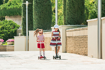 Image showing Preschooler girls riding scooter outdoors.