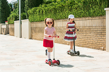 Image showing Preschooler girls riding scooter outdoors.