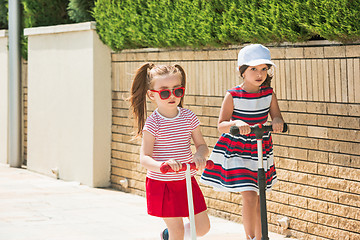 Image showing Preschooler girls riding scooter outdoors.