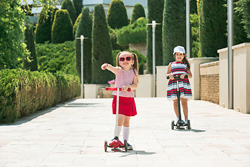 Image showing Preschooler girls riding scooter outdoors.