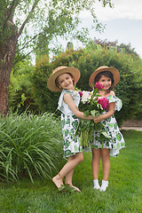 Image showing Portrait of smiling beautiful girls with bouquet of peonies against green grass at summer park.