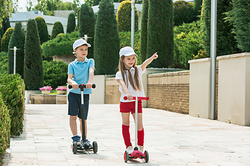 Image showing Preschooler girl and boy riding scooter outdoors.