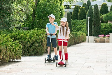 Image showing Preschooler girl and boy riding scooter outdoors.