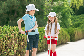 Image showing Preschooler girl and boy riding scooter outdoors.