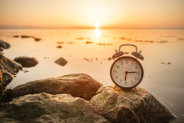 Image showing Alarm clock on a rock in the sunrise by the ocean