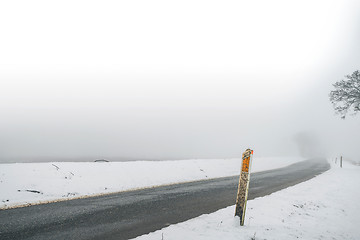 Image showing Marker post by a misty road in the winter