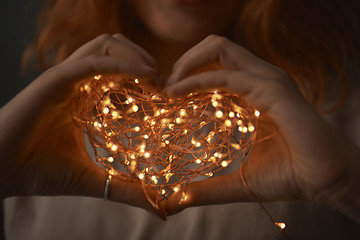 Image showing Woman hands holding string of lights in the dark.