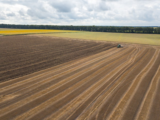 Image showing An endless agricultural field after harvesting with tractor on it against a blue cloudy sky on a summer day.