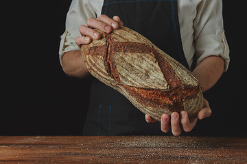 Image showing Baker\'s hands hold an oval bread.