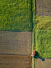 Image showing Aerial view from the drone, a bird\'s eye view of agricultural fields with a road through and a tractor on it in the spring evening at sunset