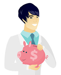 Image showing Young asian doctor holding a piggy bank.