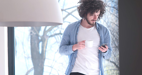 Image showing young man drinking coffee and using a mobile phone  at home