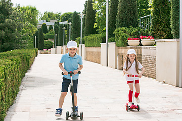 Image showing Preschooler girl and boy riding scooter outdoors.