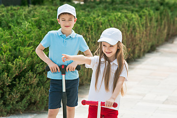 Image showing Preschooler girl and boy riding scooter outdoors.