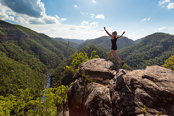 Image showing Girl leaping on high rocky cliff with mountain river backdrop