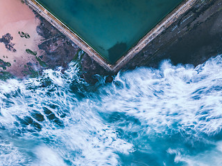 Image showing Wavs encrouch upon the rock pool like fluid fingers