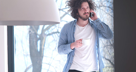 Image showing young man drinking coffee and using a mobile phone  at home