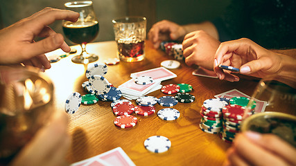 Image showing Side view photo of friends sitting at wooden table. Friends having fun while playing board game.