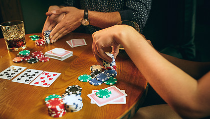 Image showing Side view photo of friends sitting at wooden table. Friends having fun while playing board game.