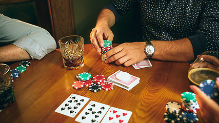 Image showing Side view photo of friends sitting at wooden table. Friends having fun while playing board game.