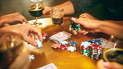 Image showing Side view photo of friends sitting at wooden table. Friends having fun while playing board game.