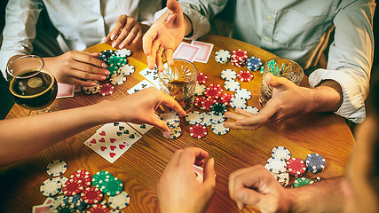 Image showing Side view photo of friends sitting at wooden table. Friends having fun while playing board game.