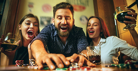 Image showing Side view photo of friends sitting at wooden table. Friends having fun while playing board game.