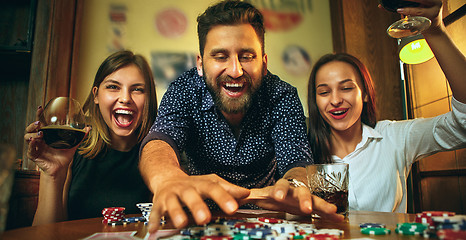 Image showing Side view photo of friends sitting at wooden table. Friends having fun while playing board game.