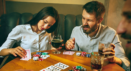 Image showing Side view photo of friends sitting at wooden table. Friends having fun while playing board game.