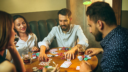 Image showing Side view photo of friends sitting at wooden table. Friends having fun while playing board game.