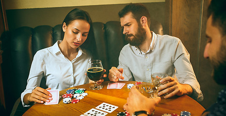 Image showing Side view photo of friends sitting at wooden table. Friends having fun while playing board game.