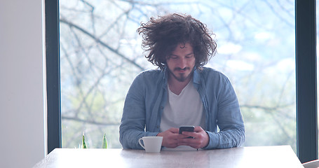 Image showing young man drinking coffee and using a mobile phone  at home