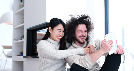 Image showing young multiethnic couple using a tablet on the floor