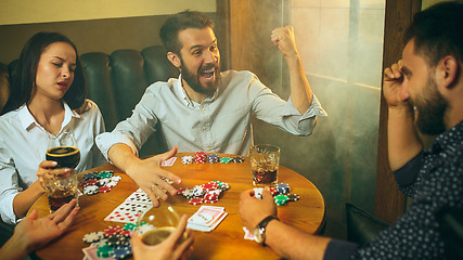 Image showing Side view photo of friends sitting at wooden table. Friends having fun while playing board game.