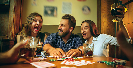 Image showing Side view photo of friends sitting at wooden table. Friends having fun while playing board game.