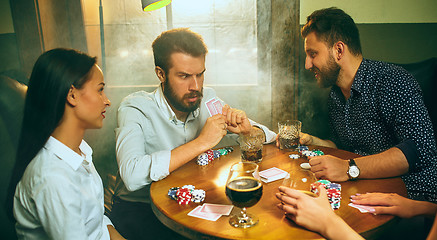 Image showing Side view photo of friends sitting at wooden table. Friends having fun while playing board game.