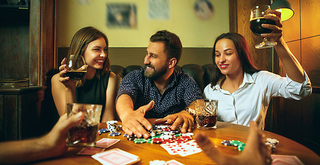 Image showing Side view photo of friends sitting at wooden table. Friends having fun while playing board game.