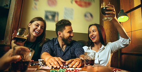 Image showing Side view photo of friends sitting at wooden table. Friends having fun while playing board game.