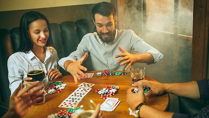 Image showing Side view photo of friends sitting at wooden table. Friends having fun while playing board game.