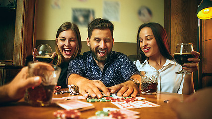 Image showing Side view photo of friends sitting at wooden table. Friends having fun while playing board game.