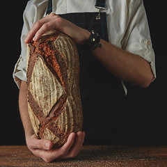 Image showing Baker\'s hands hold an oval bread.