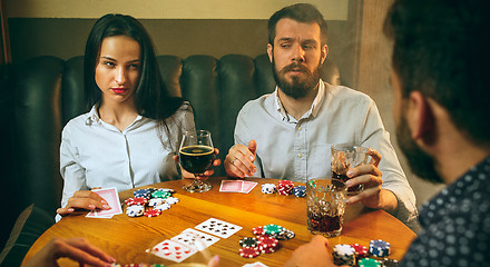 Image showing Side view photo of friends sitting at wooden table. Friends having fun while playing board game.