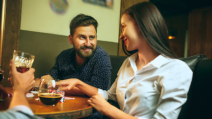 Image showing Side view photo of friends sitting at wooden table. Friends having fun while playing board game.